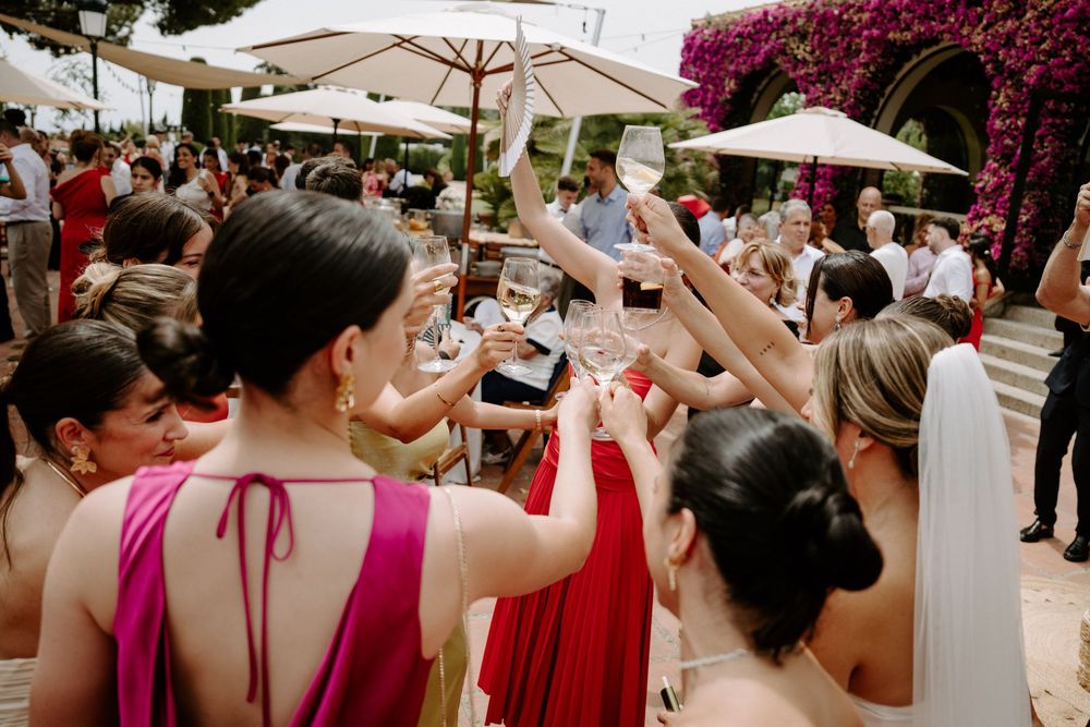 Guests raising champagne glasses in a toast at an outdoor wedding reception with white umbrellas and pink flowers.