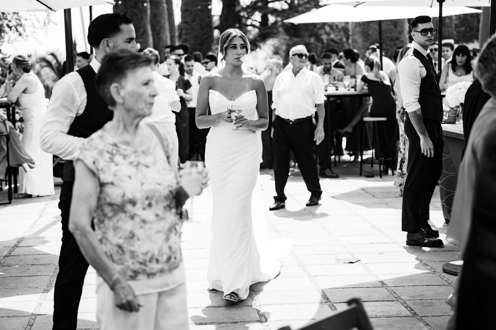Bride in white gown dances with elderly guest at outdoor wedding reception celebration.