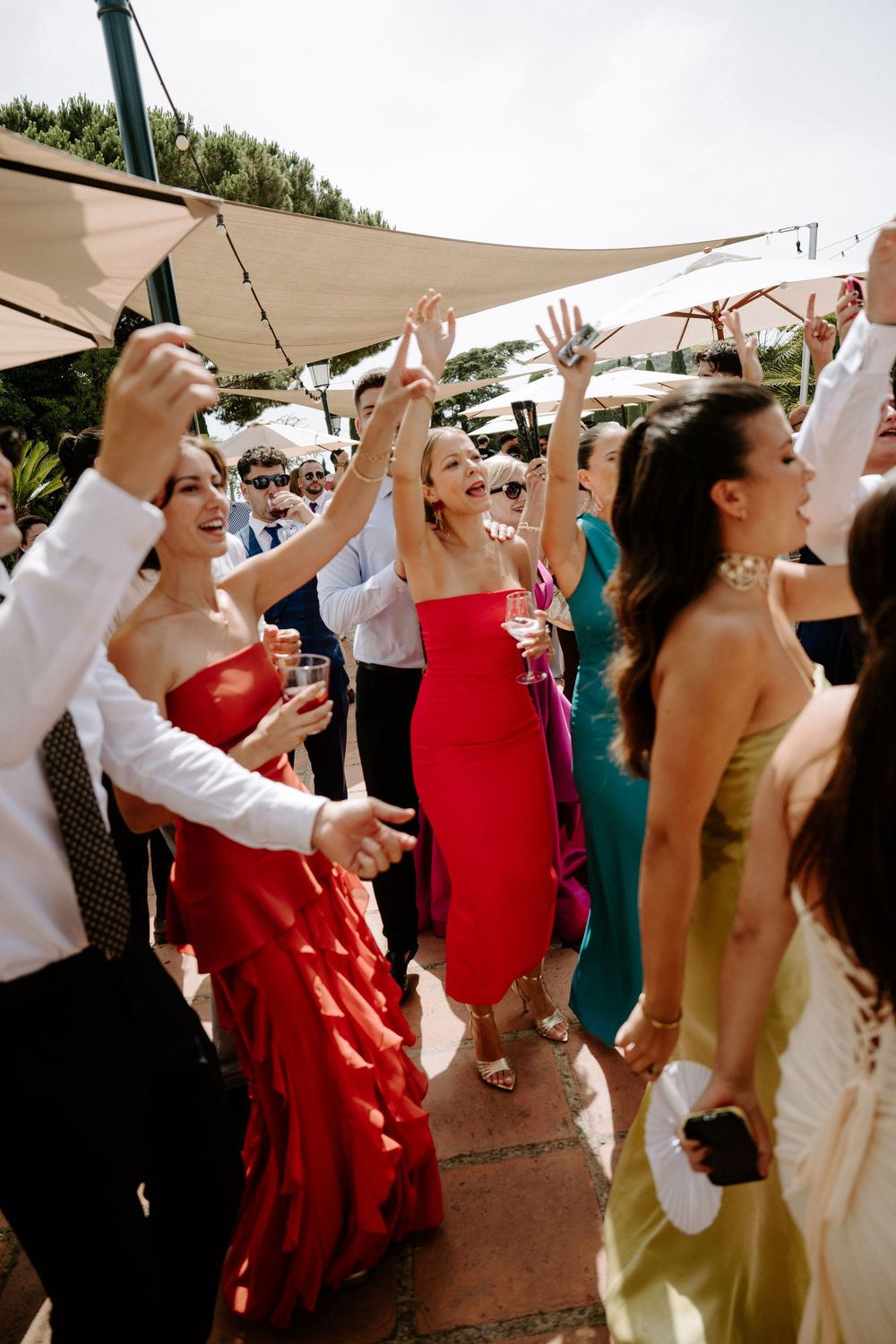 Guests in colorful formal dresses dancing and celebrating outdoors at a wedding reception.