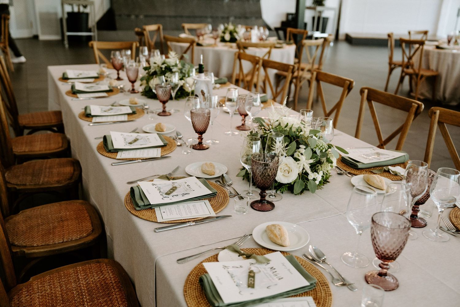 Elegant wedding reception table with floral centerpieces, wicker chargers, pink goblets, and white linen runner.