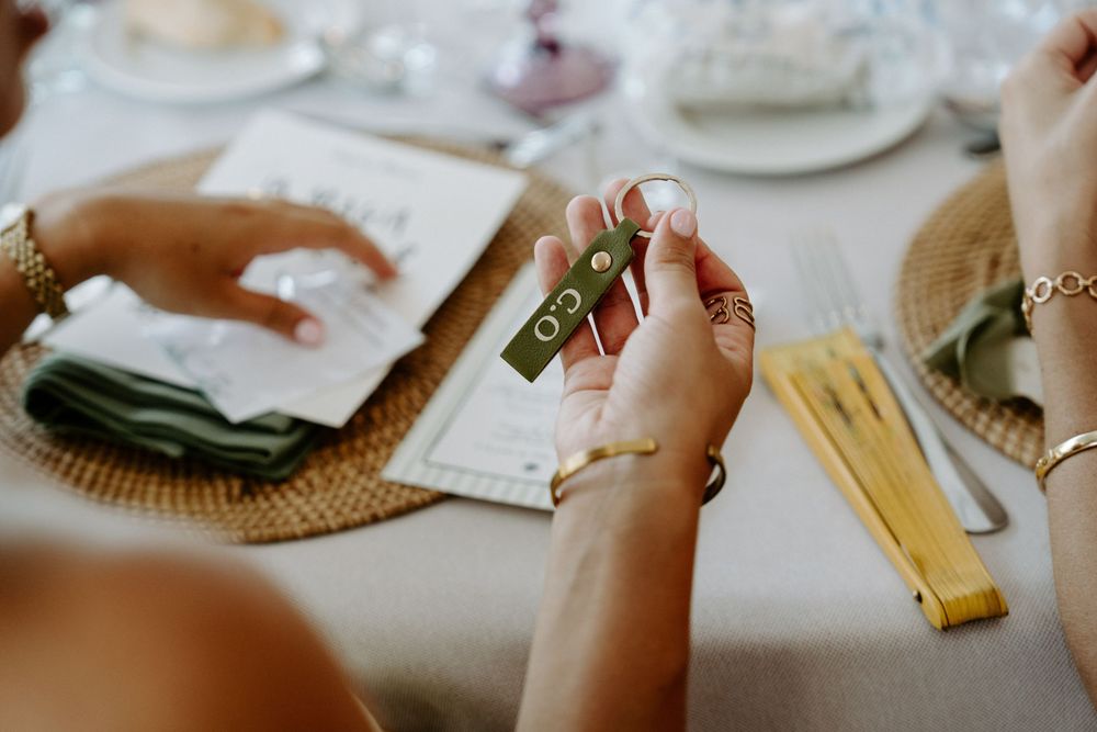 Guest holds olive green wedding favor at elegantly set reception table with gold cutlery.