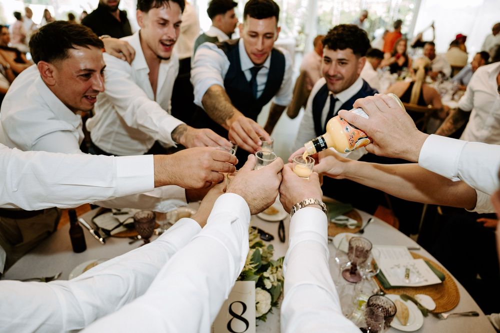 Groomsmen clinking glasses together in a celebratory toast at a wedding reception dinner table.