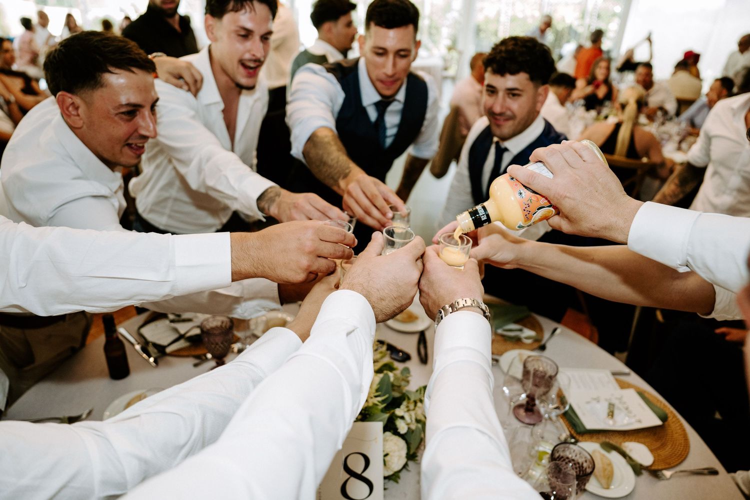 Groomsmen clinking glasses together in a celebratory toast at a wedding reception dinner table.