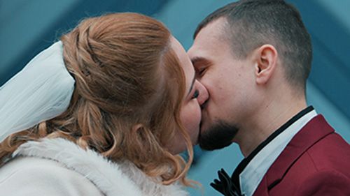 Bride and groom share their first kiss at an outdoor wedding ceremony under a white floral arch.