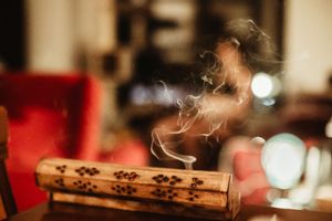 Wooden incense burner with smoke curling upward on a table, red chairs blurred in the background.