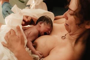 Newborn baby placed on mother's chest immediately after birth during skin-to-skin contact in delivery room.