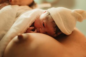 Newborn baby wrapped in white towel resting on mother's chest during skin-to-skin contact after birth.