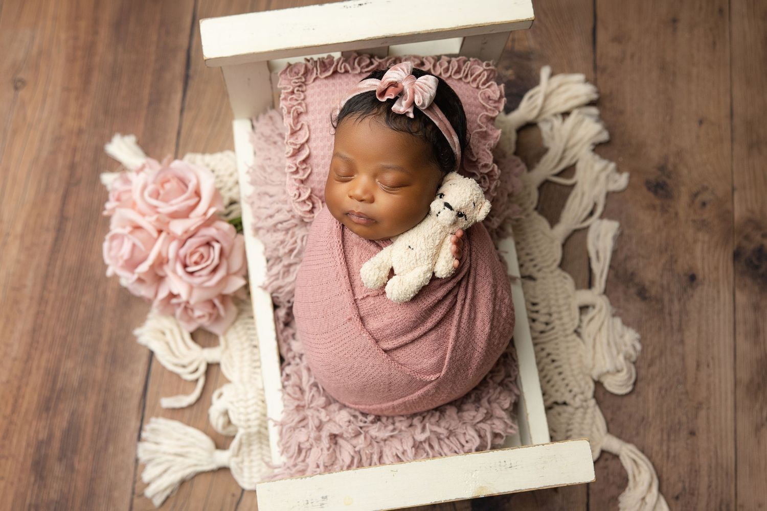 Peaceful newborn baby swaddled in cream wrap sleeping on soft beige blanket during professional newborn photography session.