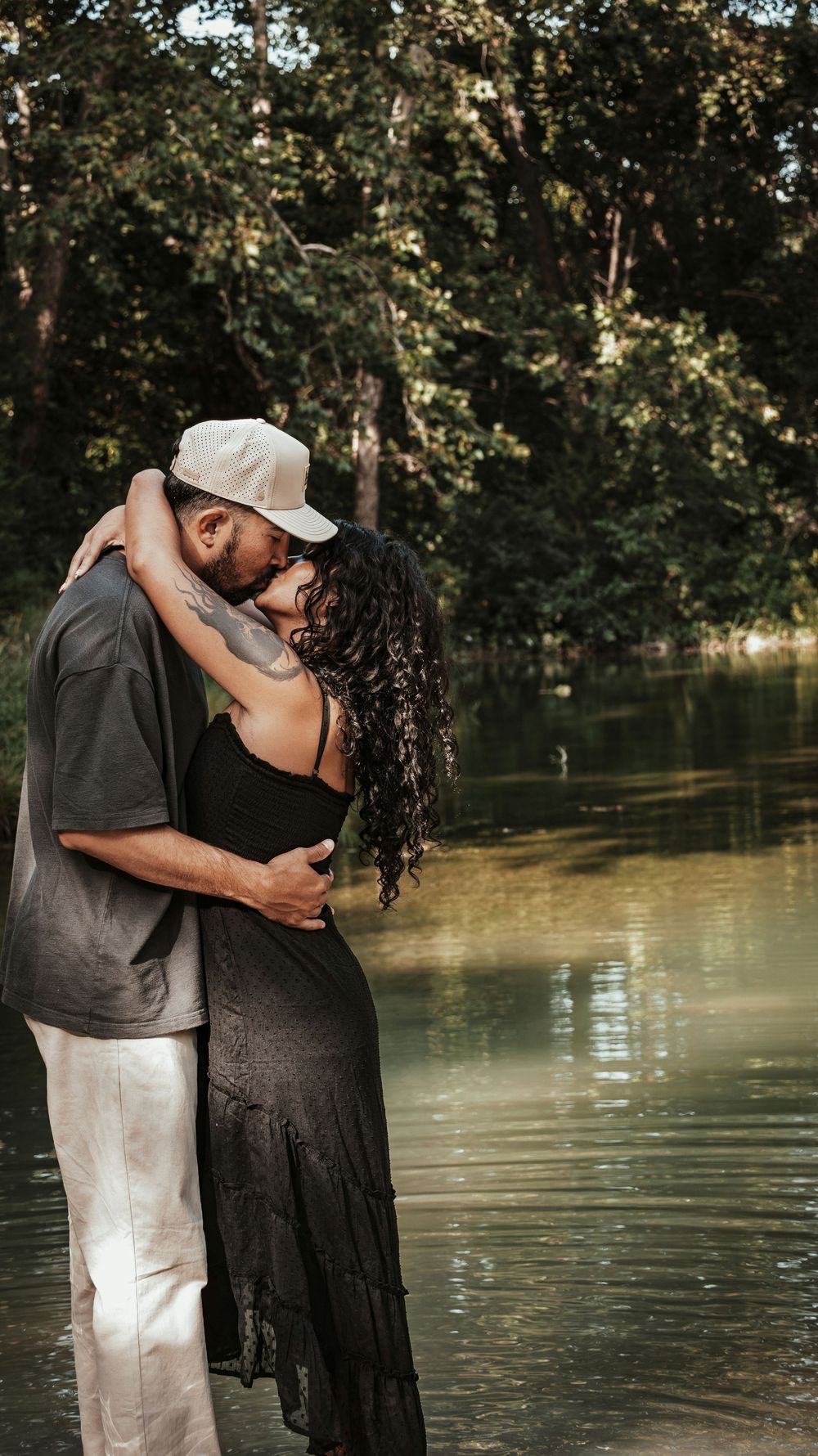 Couple embracing romantically while standing in a serene flooded forest with lush green trees reflecting on calm water.