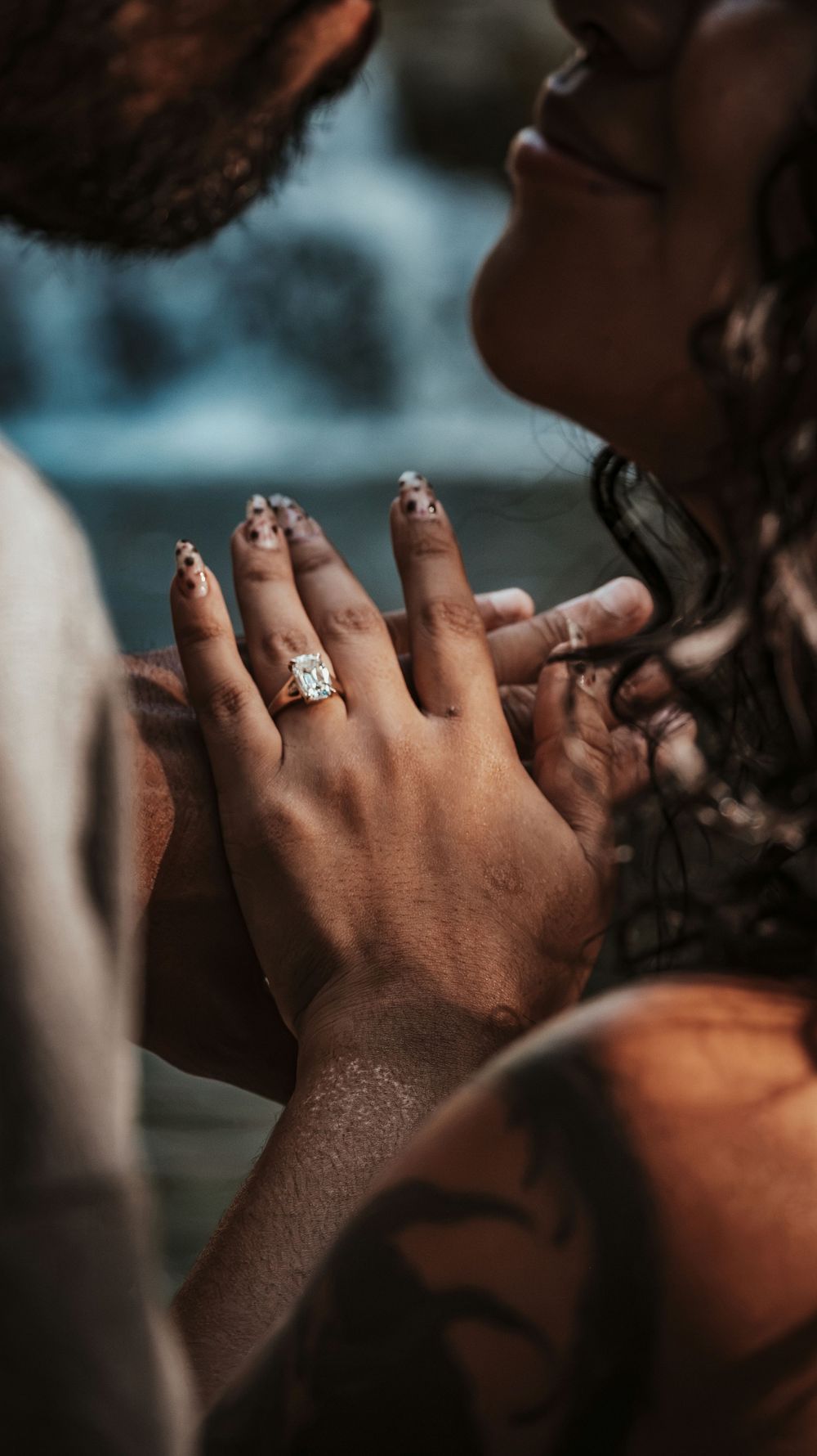 Close-up of a woman's hand displaying a sparkling diamond engagement ring while a couple shares an intimate moment.
