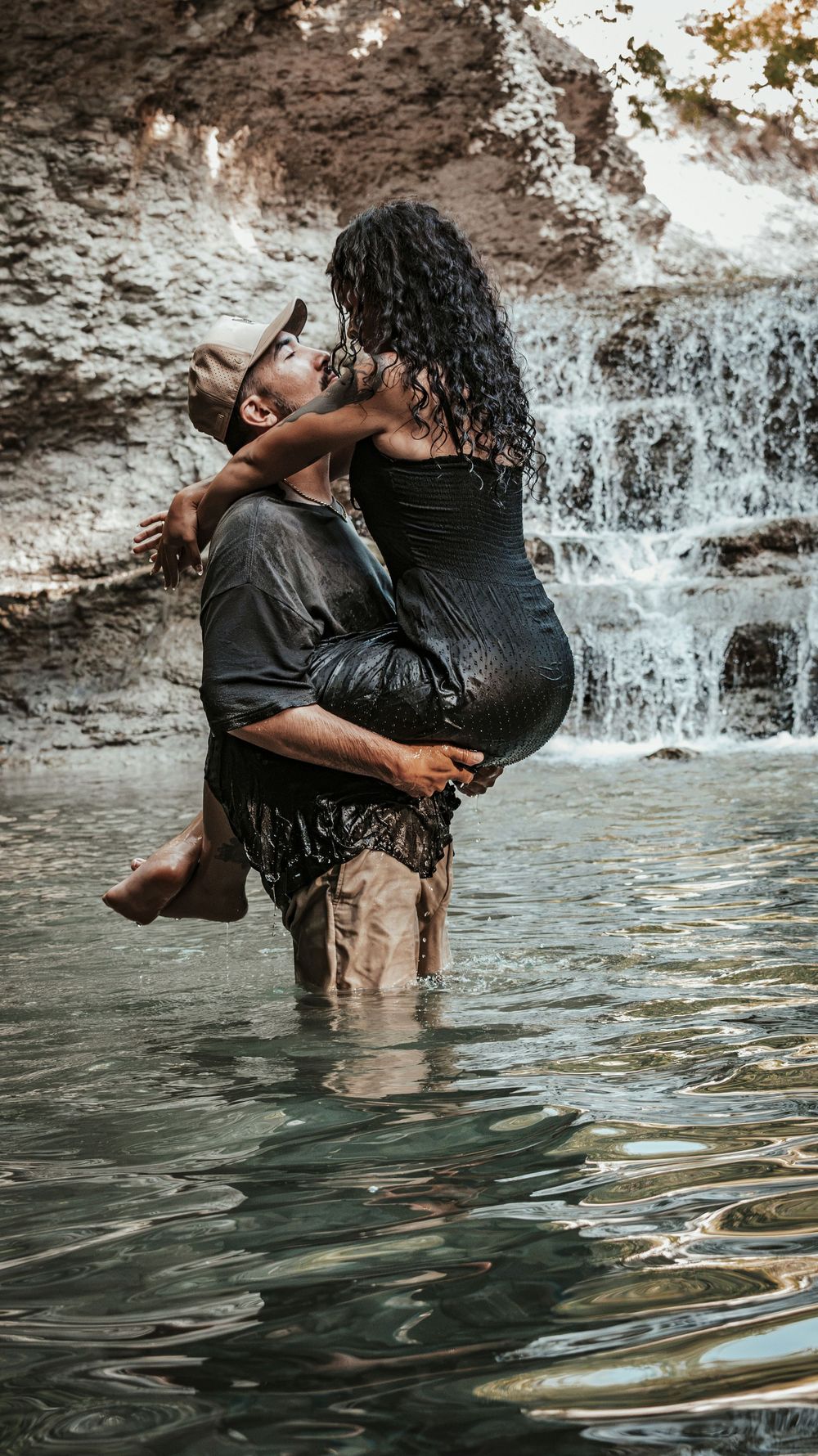 A couple shares a passionate kiss as the man lifts the woman near a scenic waterfall.