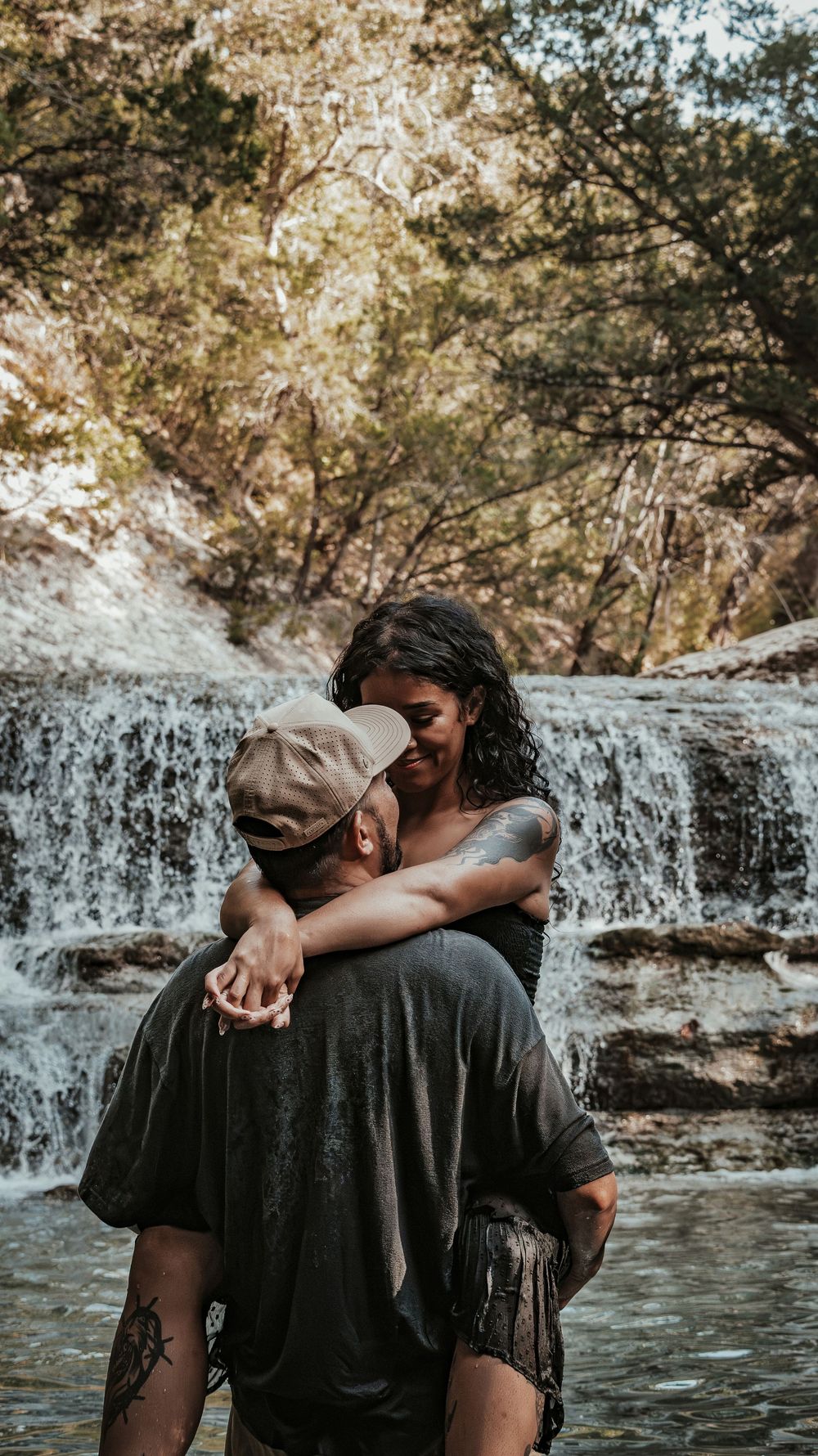 Couple embracing lovingly in a shallow river with a scenic waterfall backdrop in nature.
