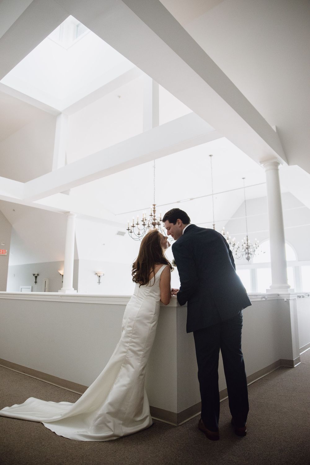Romantic wedding moment captured in modern white interior with dramatic ceiling angles.