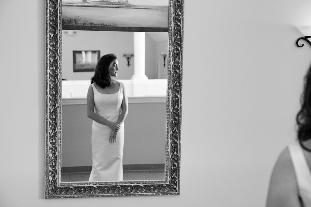 Black and white artistic reflection of bridal preparations in ornate framed mirror.