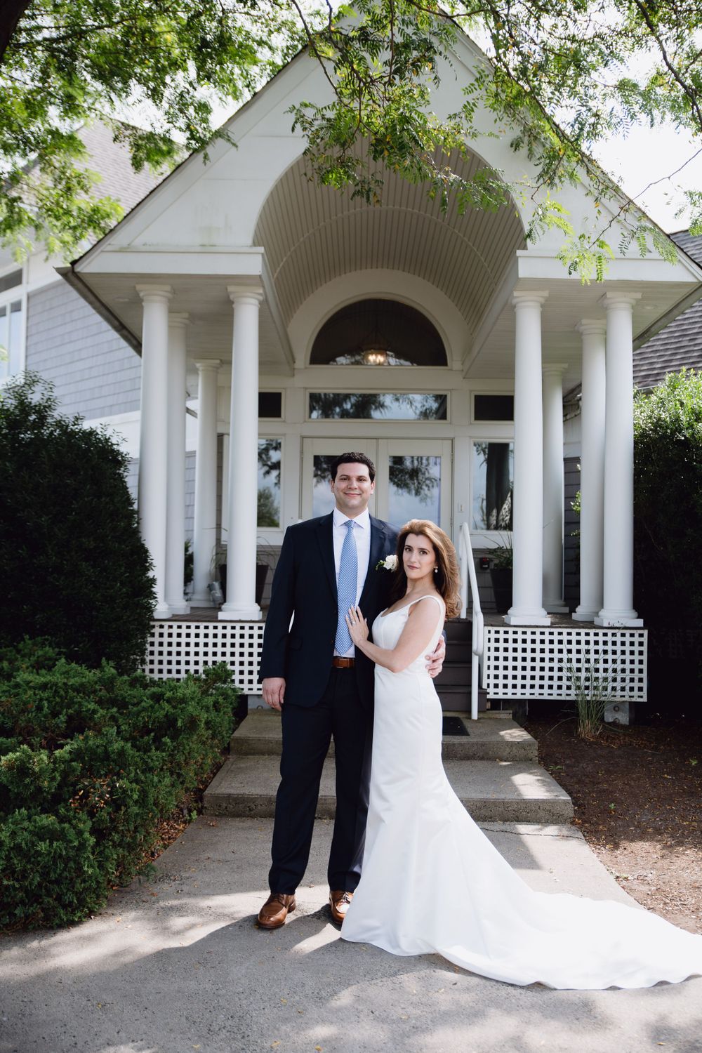 Wedding couple posed in front of classic white chapel entrance with columns.