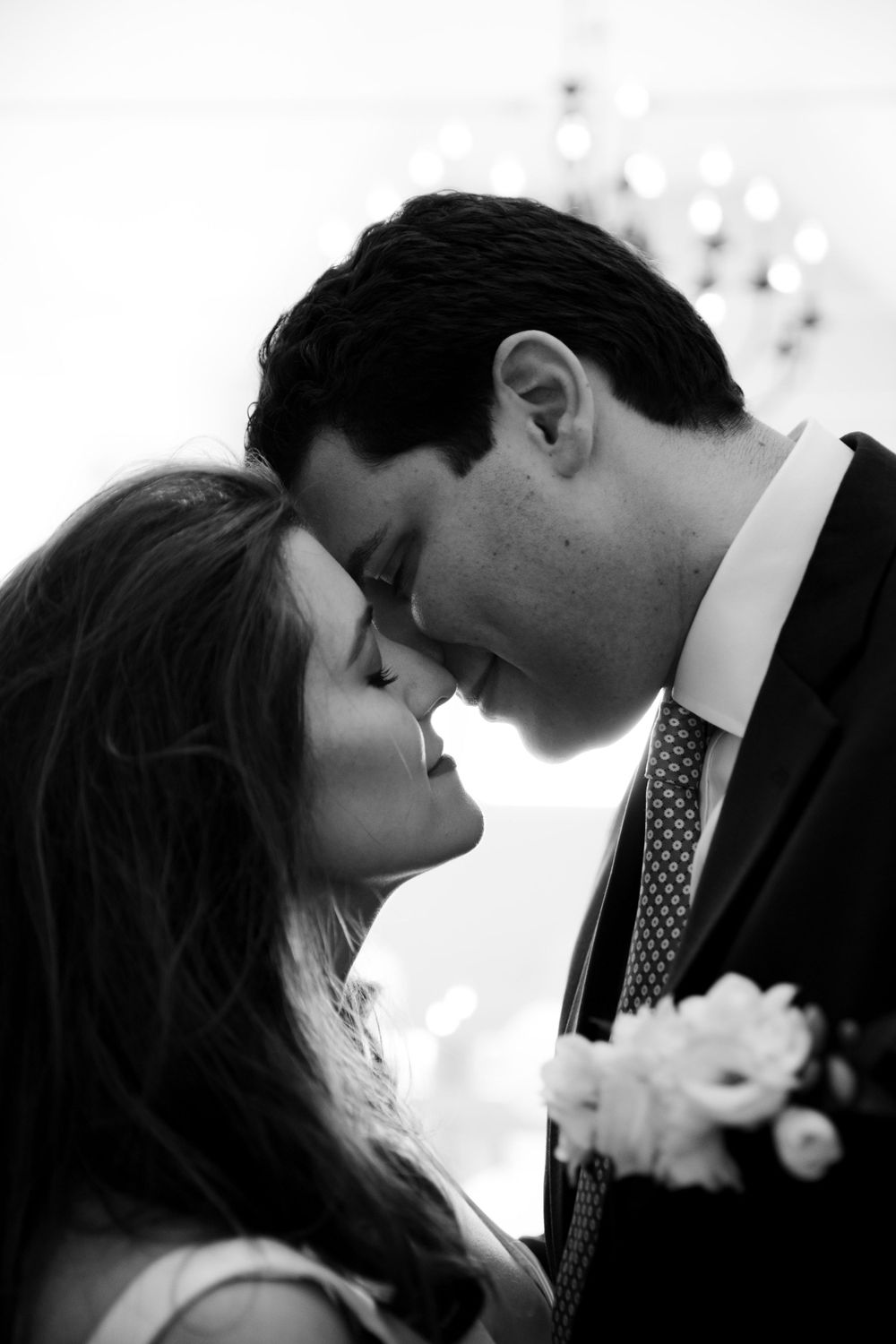 A romantic black and white photo of a couple sharing an intimate moment at what appears to be their wedding.