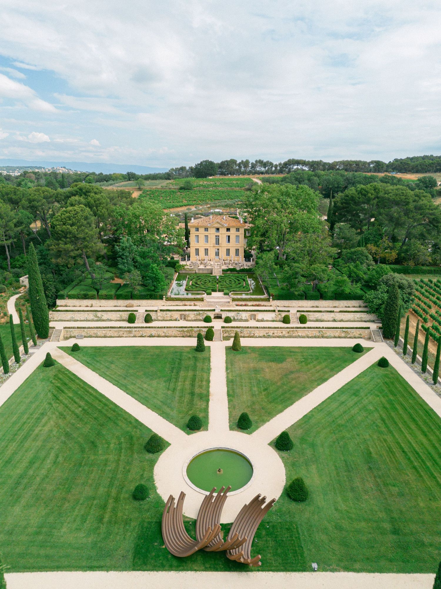 Aerial view of a grand French estate with formal gardens, manicured lawns, and a classical villa surrounded by lush greenery.