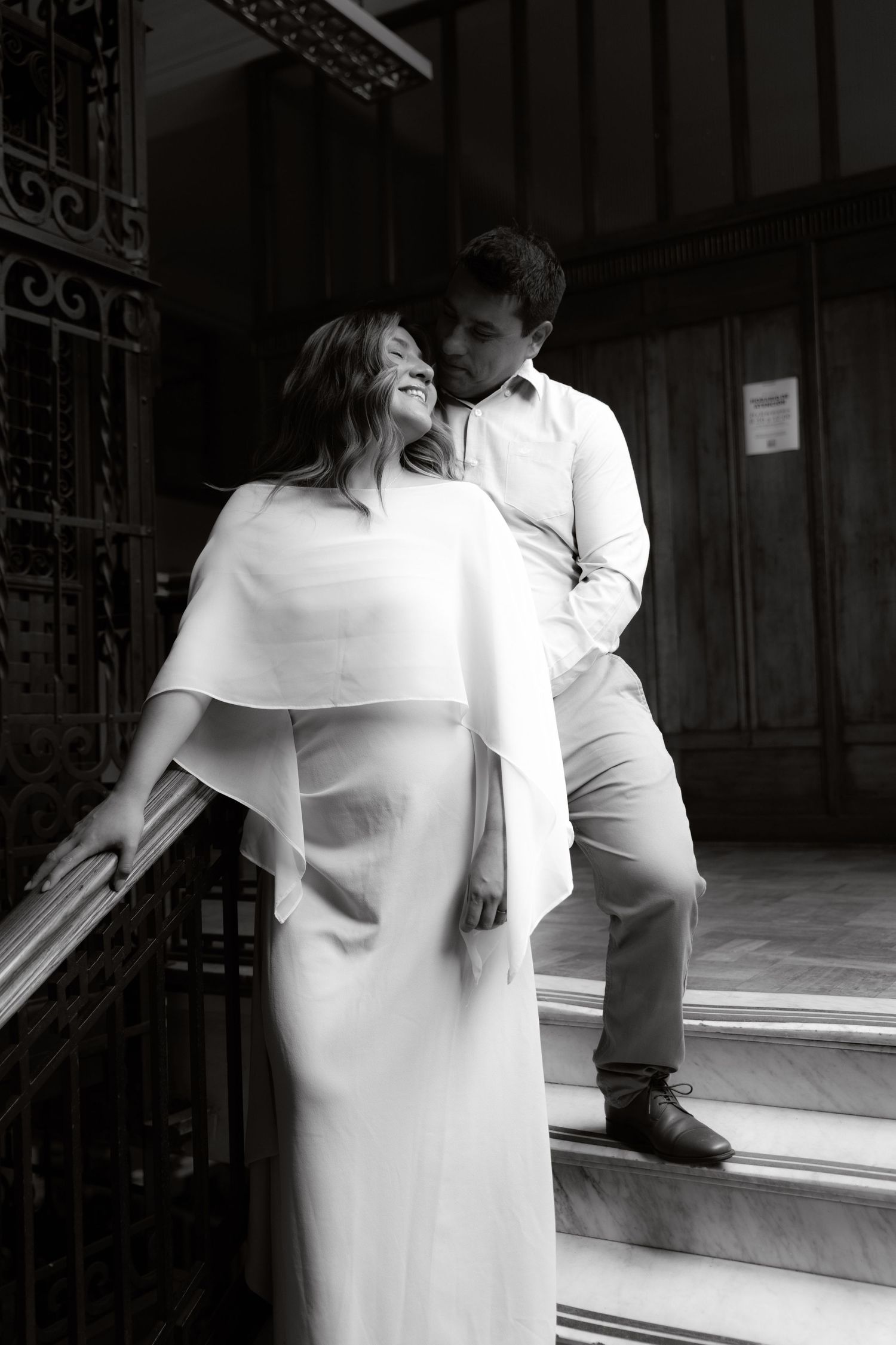 Black and white photo of romantic couple on stone steps near ornate iron gate.