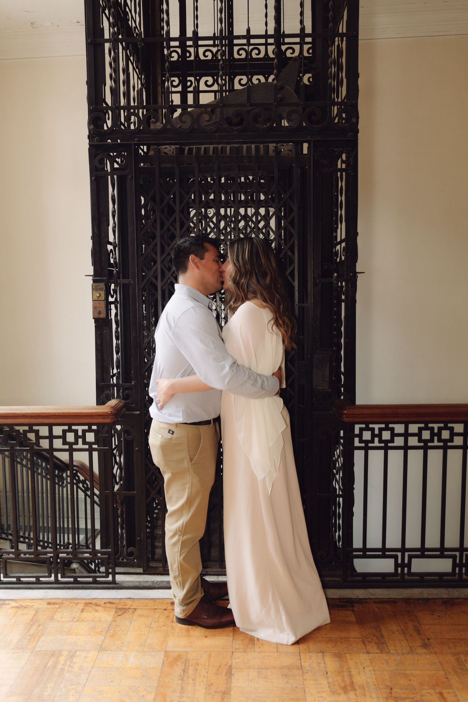 Couple sharing a kiss in front of ornate black iron gate doors on a wooden floor.