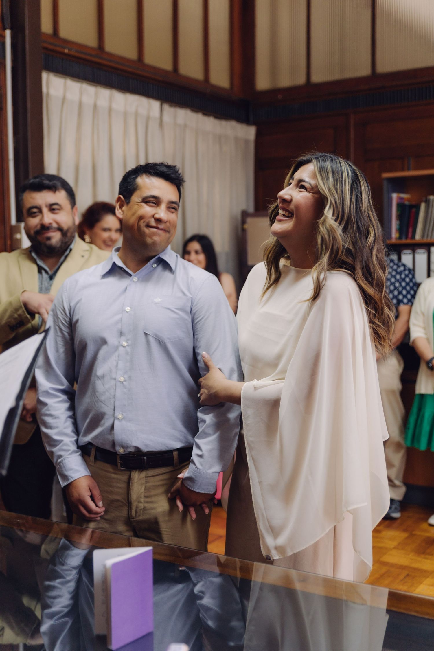 Joyful couple laughing together during civil wedding ceremony surrounded by smiling guests indoors.