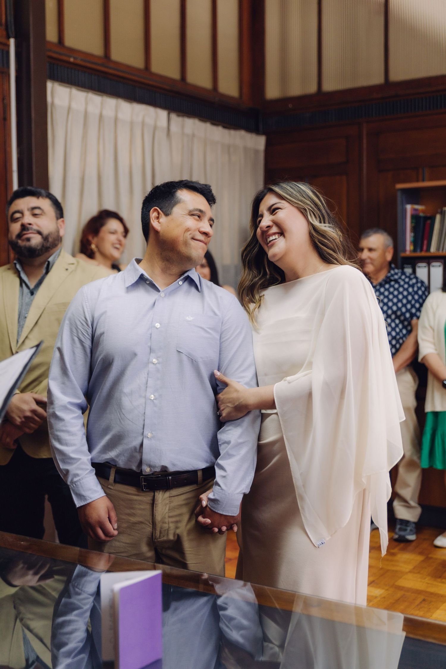 Couple exchanging loving glances and holding hands during civil wedding ceremony indoors.