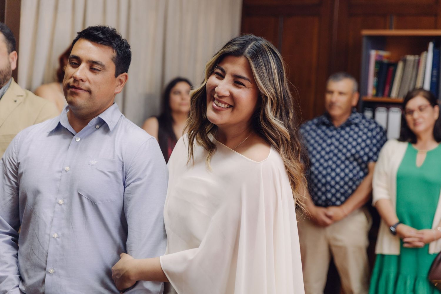 Bride smiling joyfully beside groom during civil wedding ceremony with guests watching.