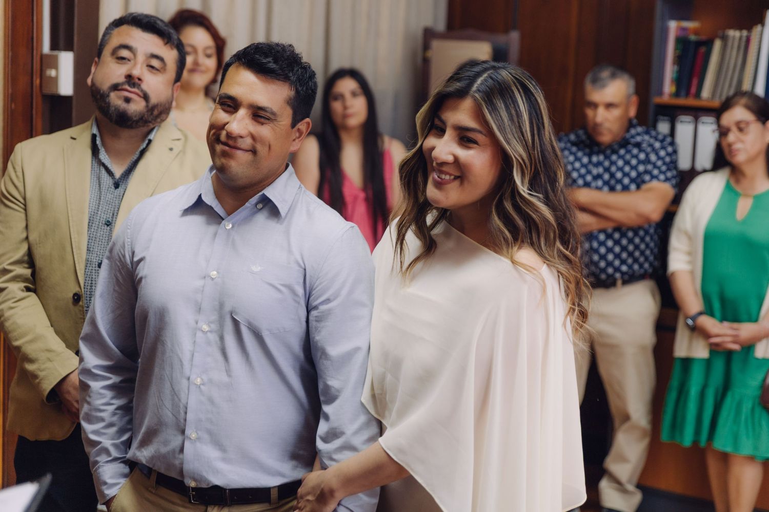 Smiling couple holding hands at civil wedding ceremony with guests standing in background.