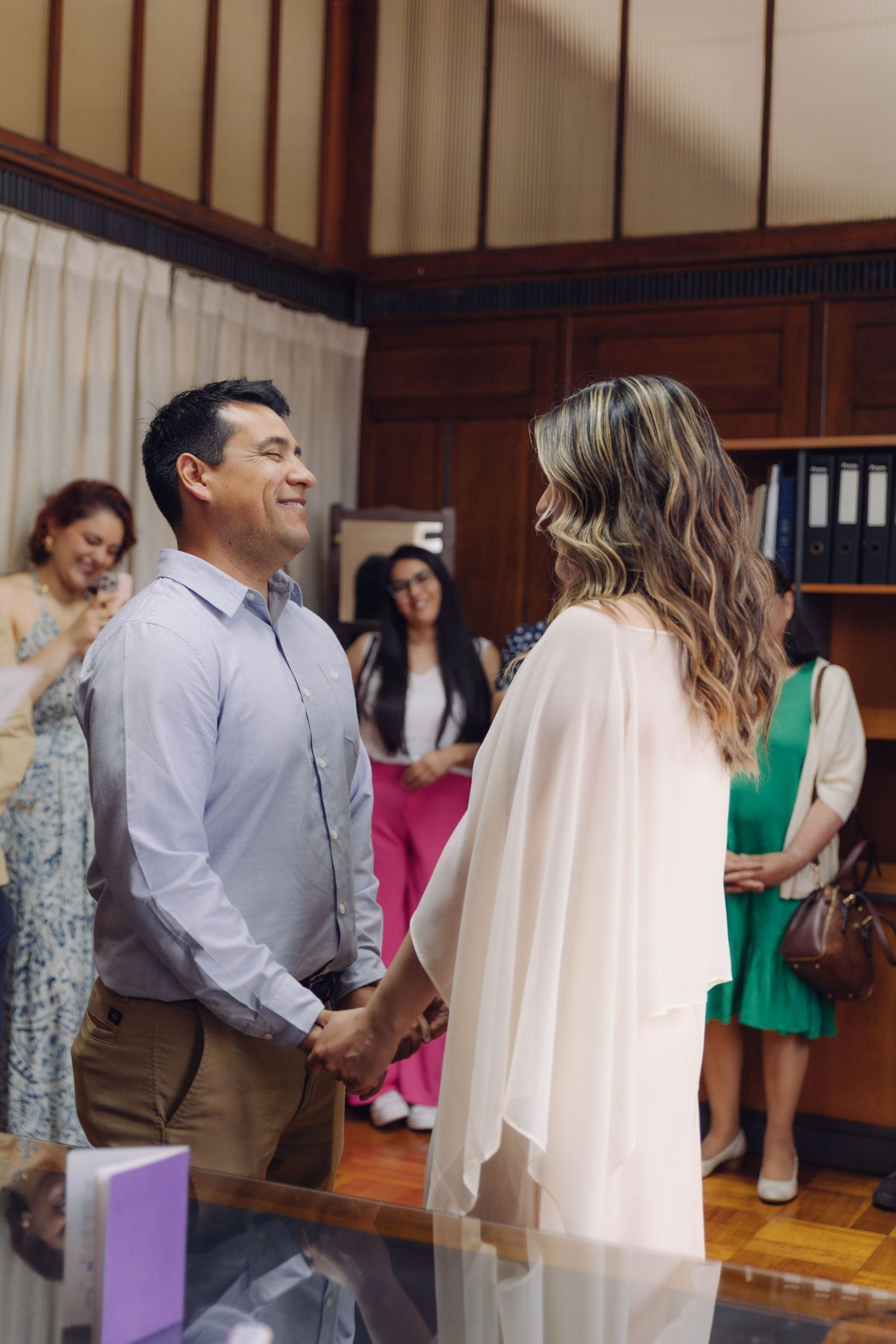 Couple holding hands and smiling at each other during an intimate civil wedding ceremony indoors.