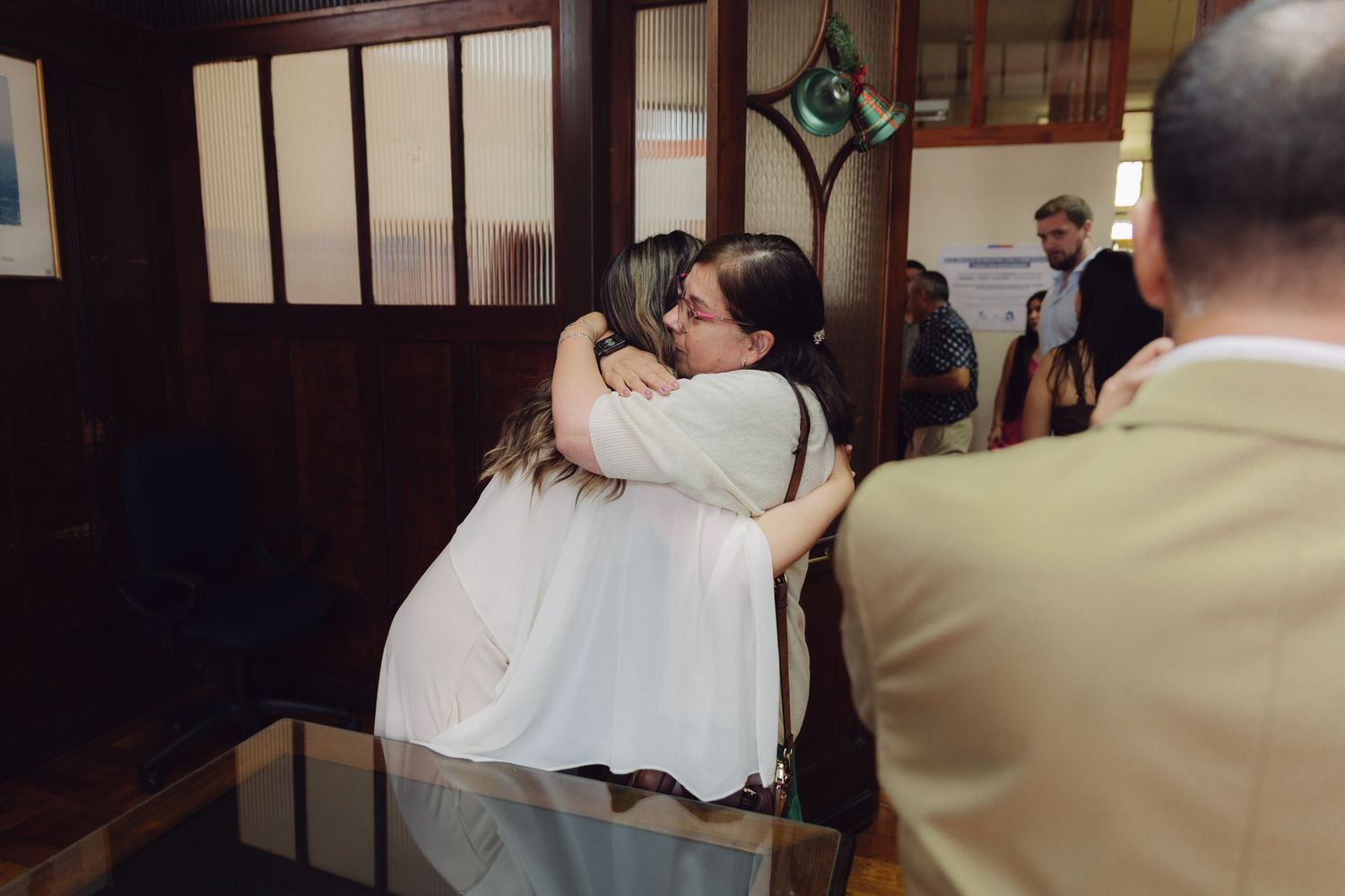 Two women share a warm embrace inside a wooden chapel during a wedding ceremony.