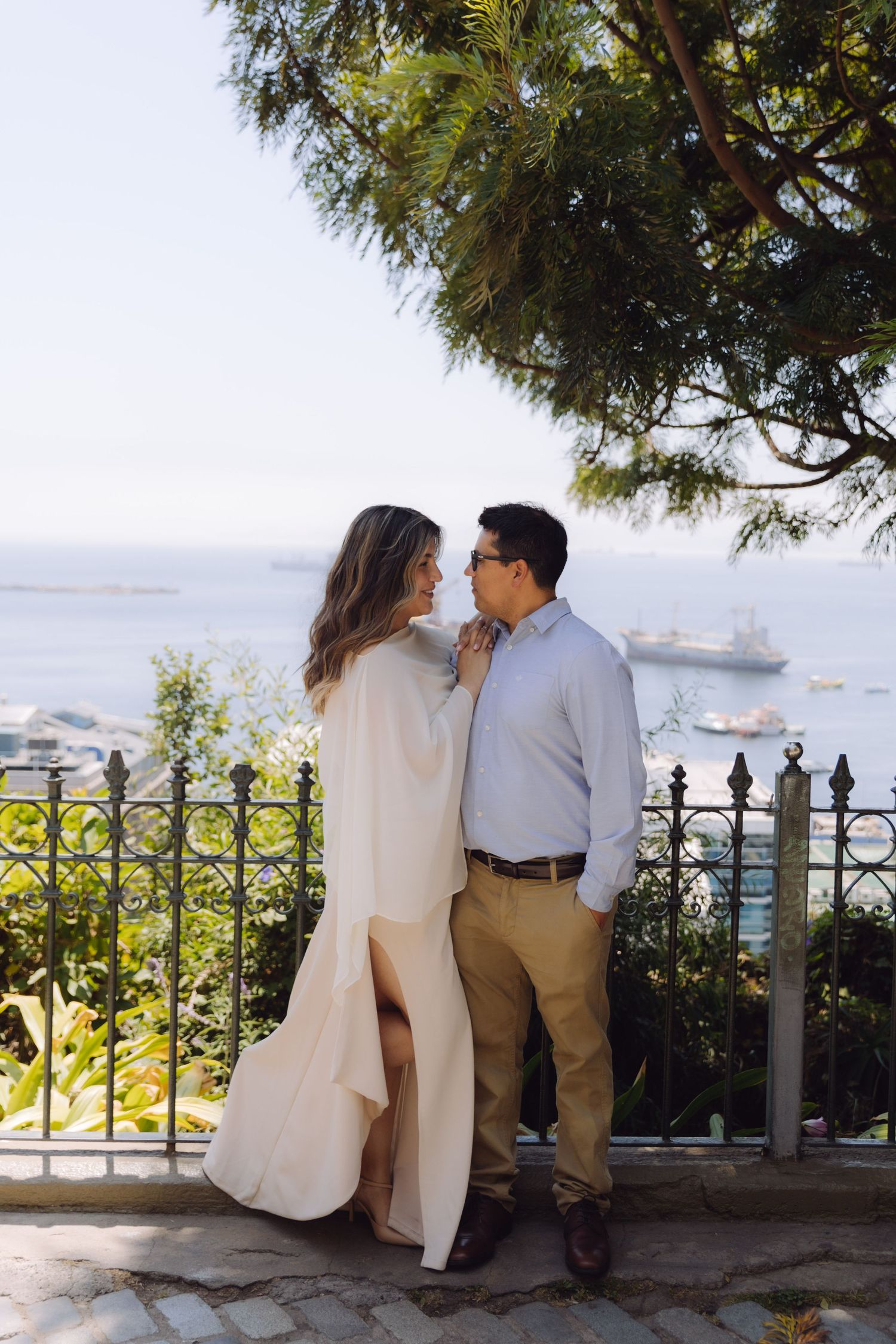 A romantic couple gazes at each other on a scenic overlook with ocean views behind them.