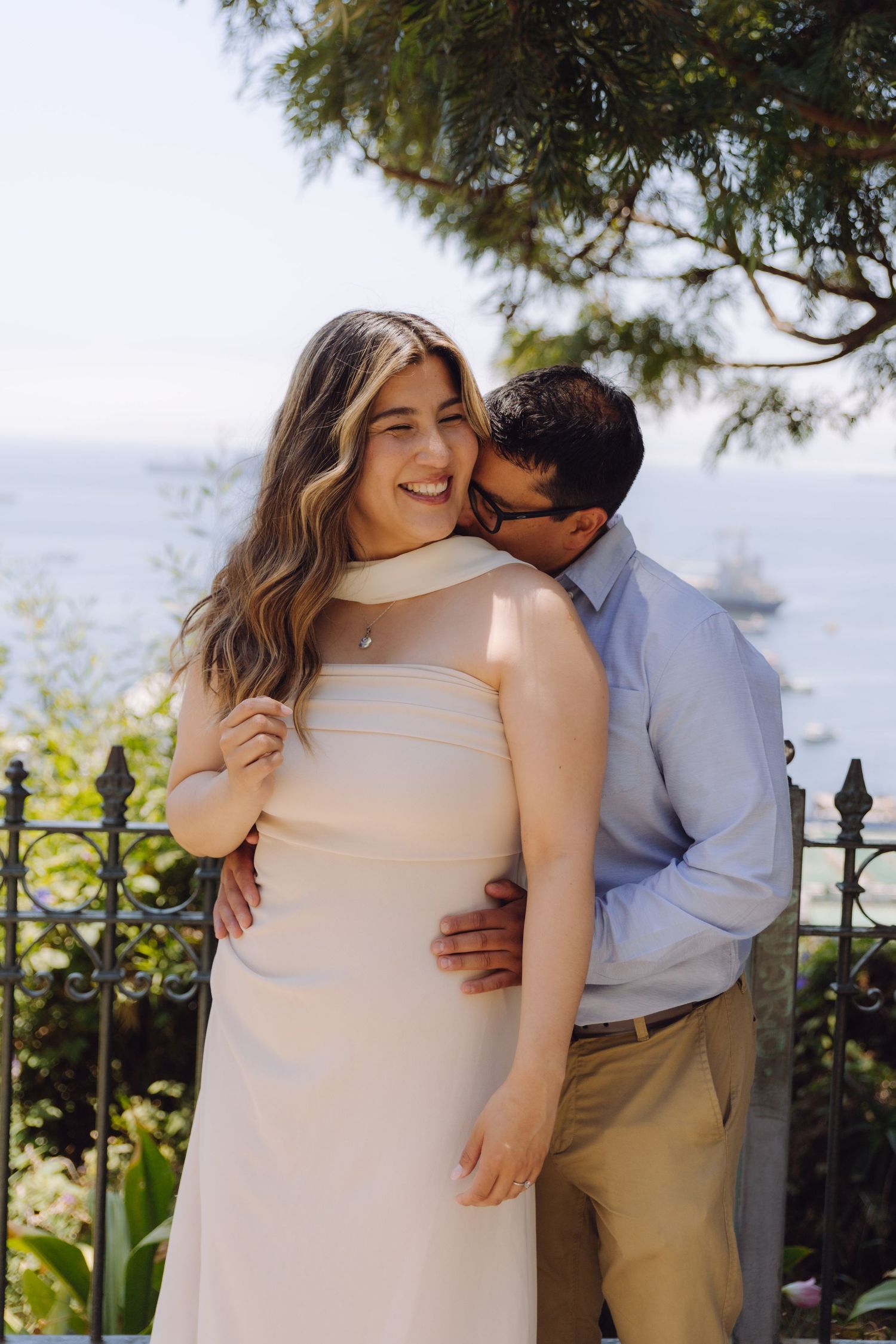 A happy couple poses romantically at a scenic overlook with blue ocean views in background.