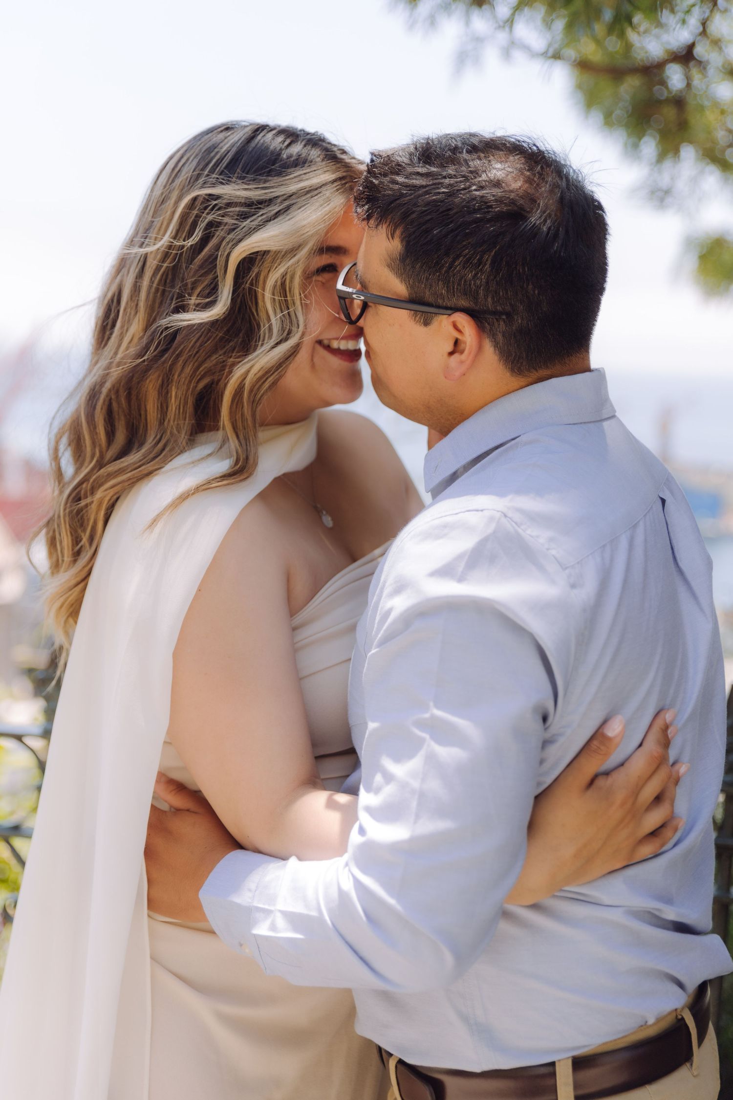 Happy couple embracing and nearly kissing outdoors with scenic waterfront background on sunny day.