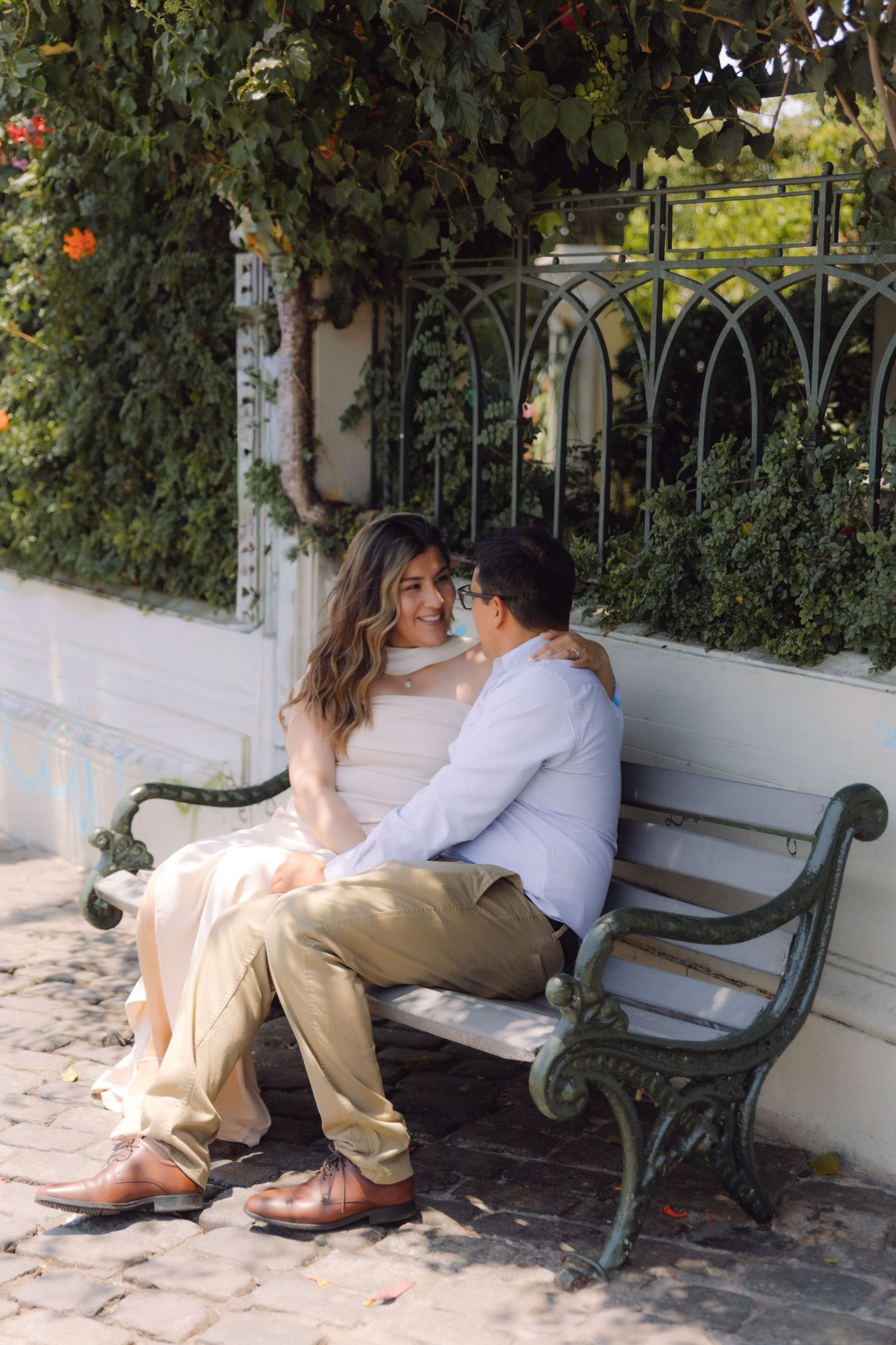 Romantic couple sitting close together on vintage green bench surrounded by lush garden greenery.