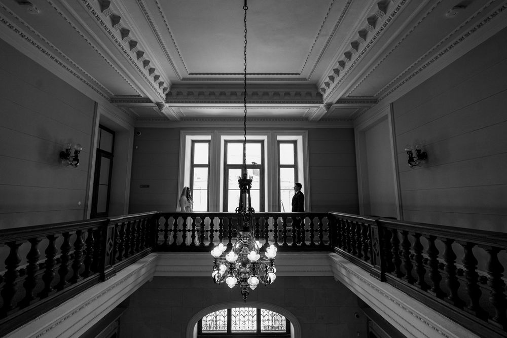 Black and white photo of an elegant grand staircase with chandelier and ornate railings in a historic building.