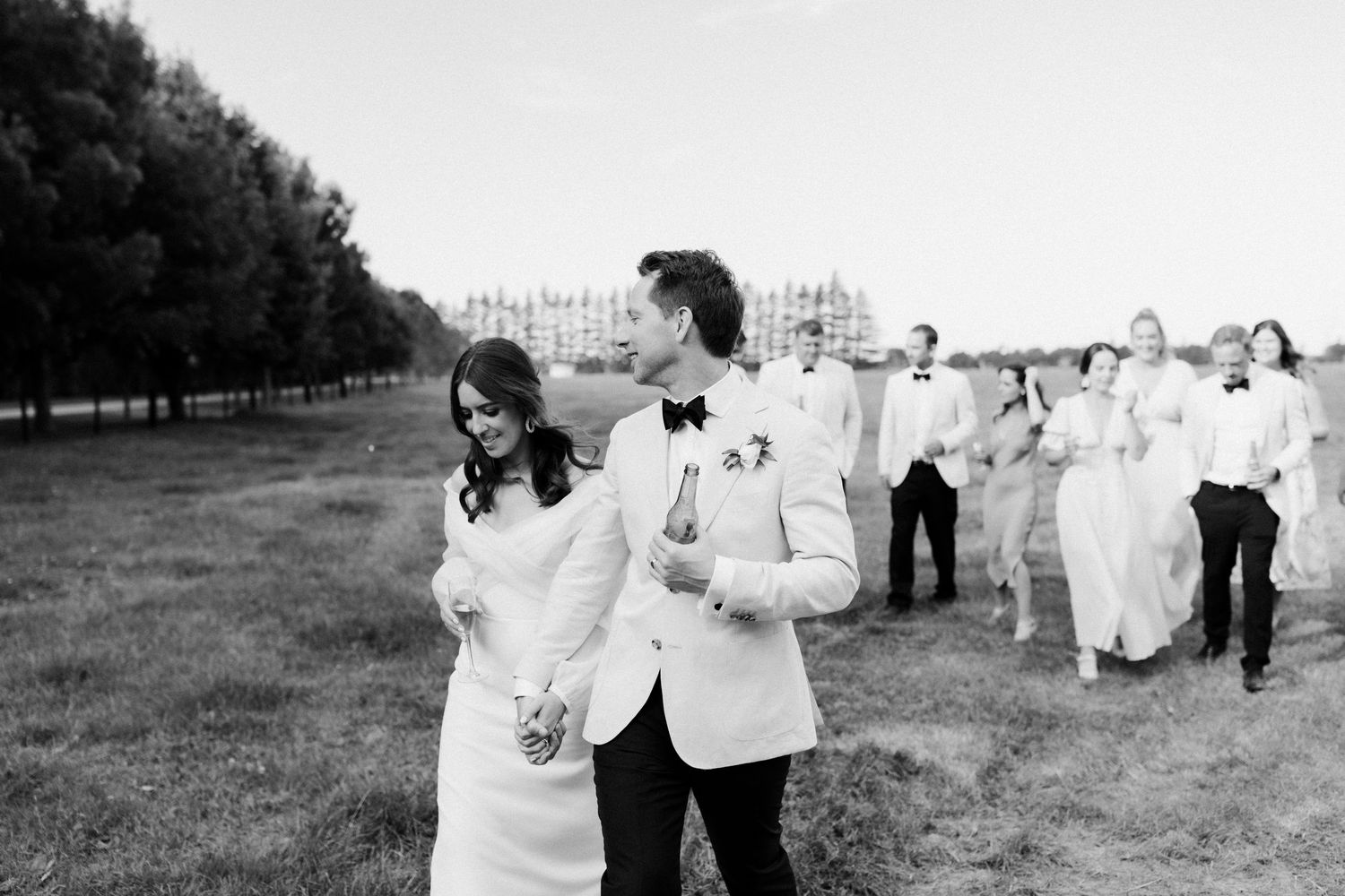 Black and white photo of wedding party walking in line across grassy field.