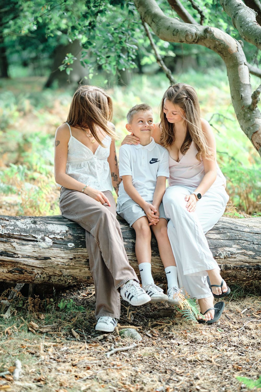 A mother and two children sit together on a fallen log in a lush green forest, sharing a warm family moment.