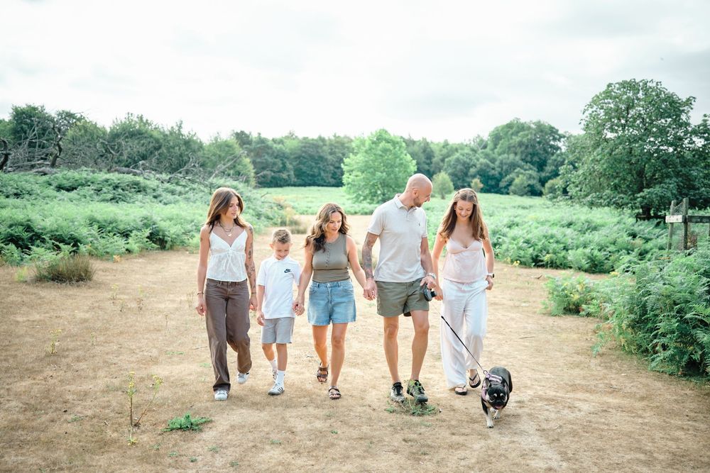 Family of five walking a dog through a scenic green park on a sunny day.