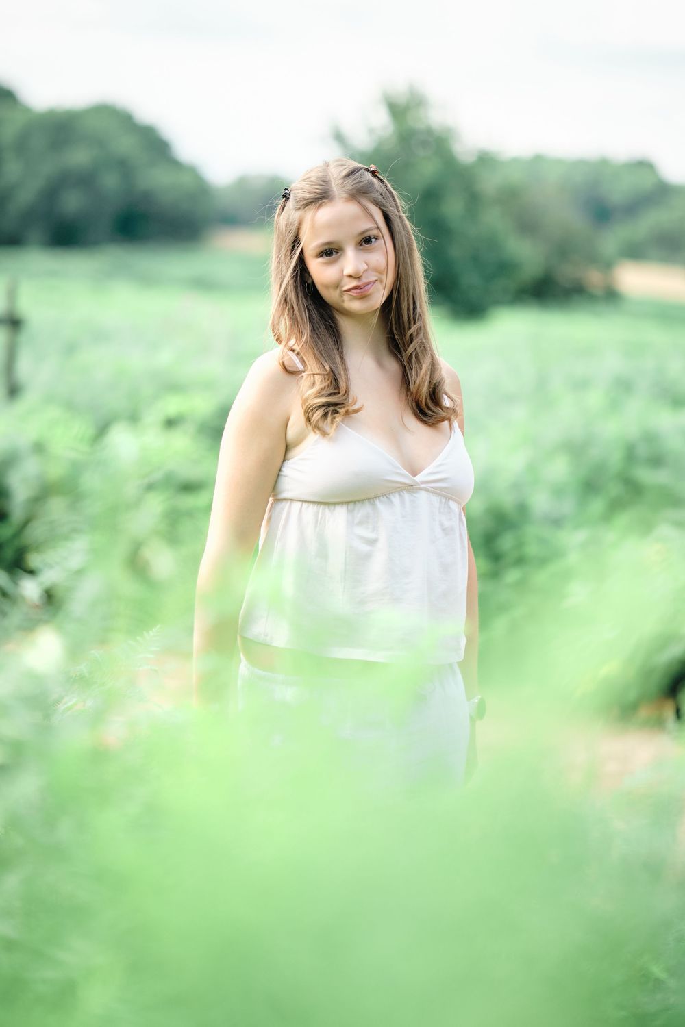 Young woman in white sundress standing in lush green field, portrait photography outdoors.