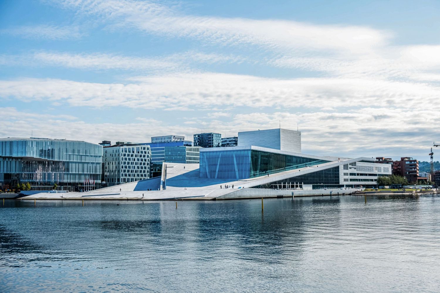 Moderní architektura na nábřeží v Oslu s budovou opery a městskou zástavbou v pozadí.