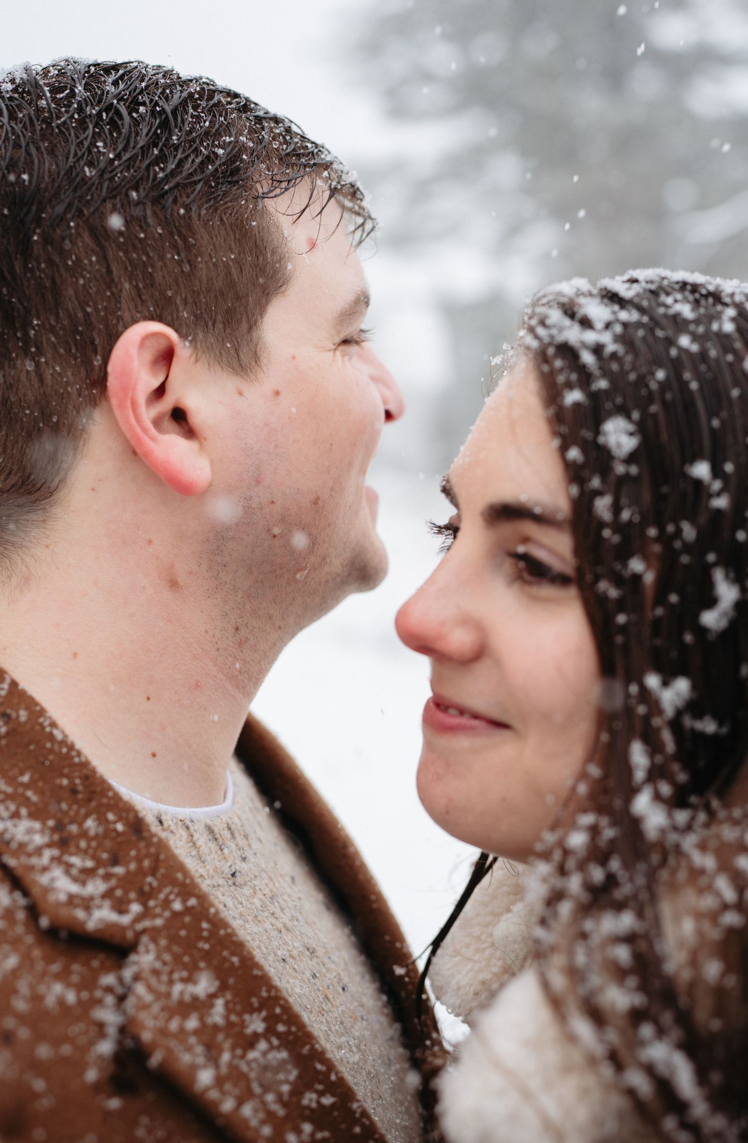 Romantic close-up of couple gazing at each other in falling snow, faces nearly touching in tender winter moment.