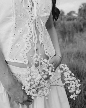 Black and white close-up of pregnant woman in white eyelet dress holding baby's breath flowers.