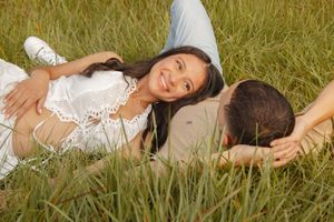 Pregnant couple lying in tall grass smiling at each other during golden hour maternity session.