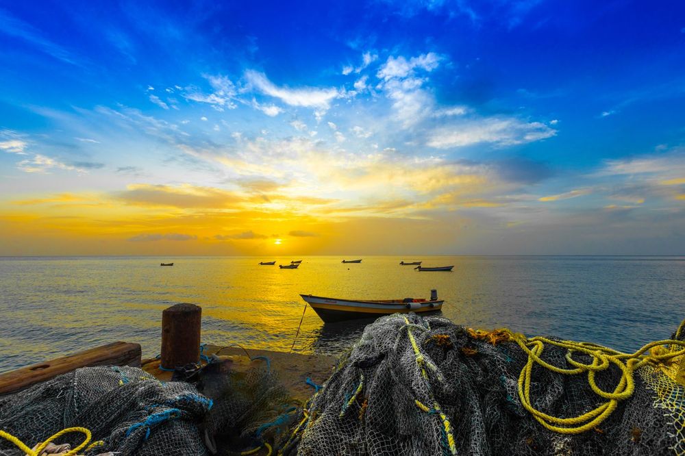 Stunning tropical sunset over the Caribbean Sea in St. Lucia featuring small fishing boats anchored near a rustic coastline.