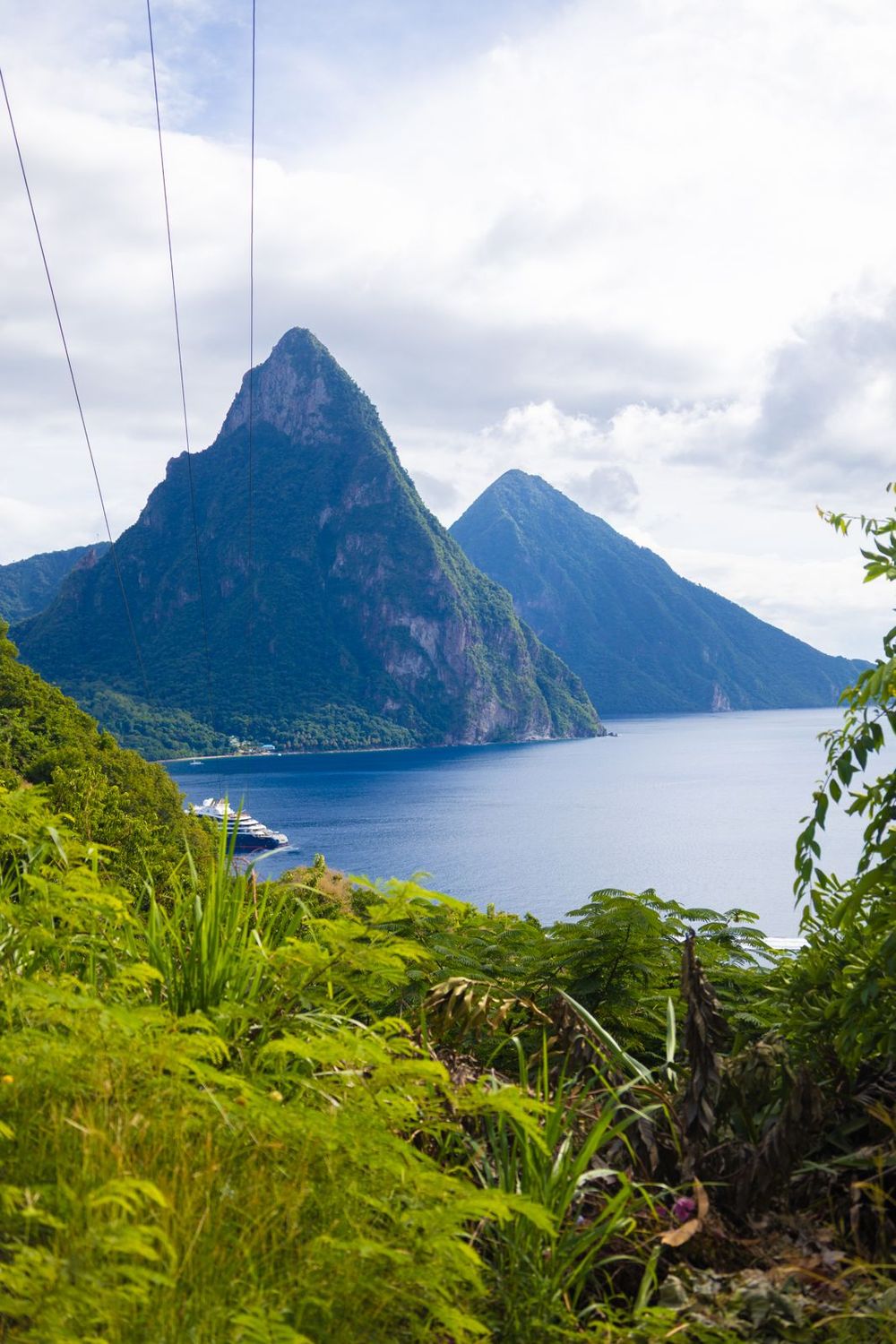 Lush tropical vegetation framing iconic twin Piton peaks with cruise ship and Caribbean Sea below.