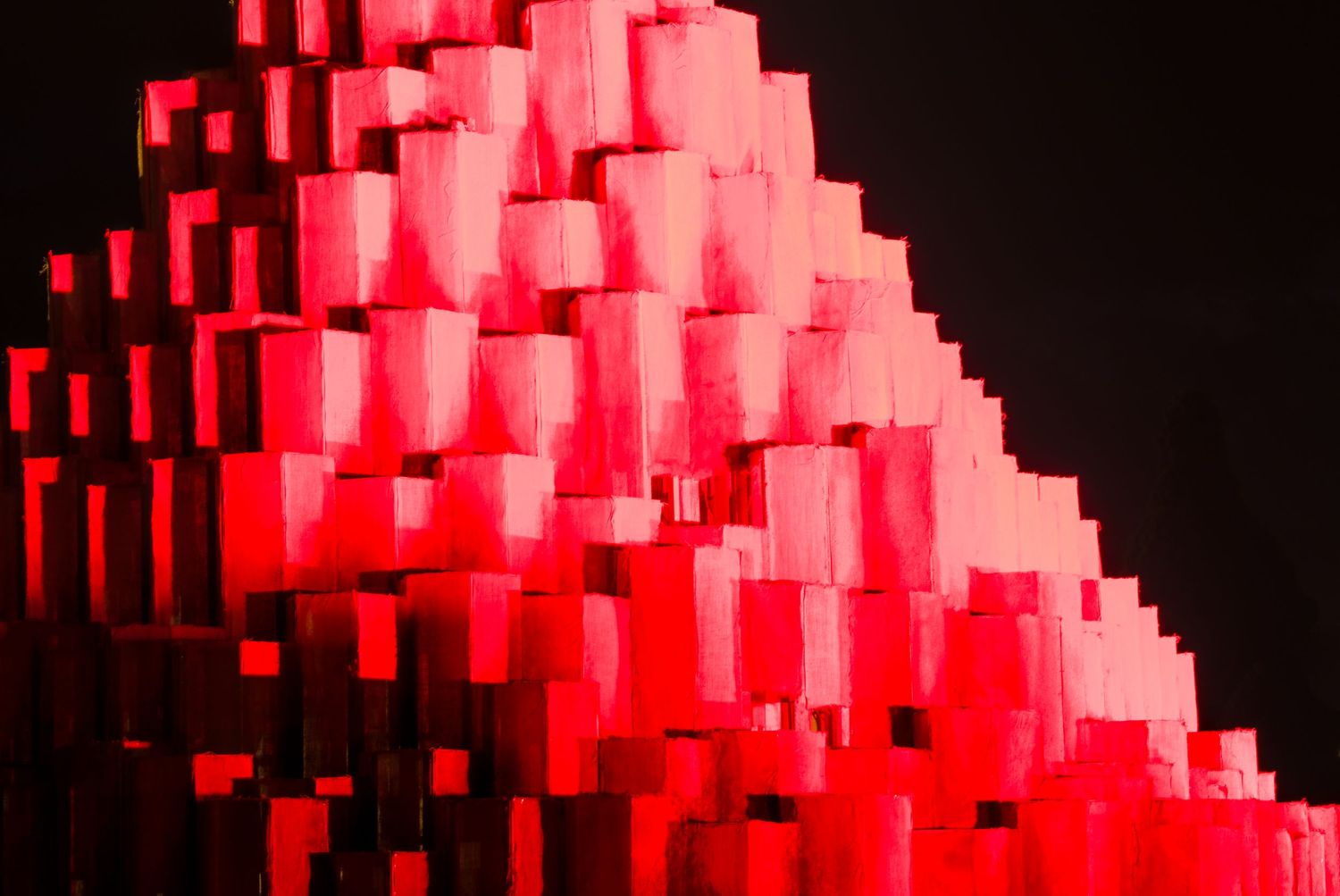 Abstract pyramid of glowing red and pink 3D blocks arranged in tiers against a dark black background.