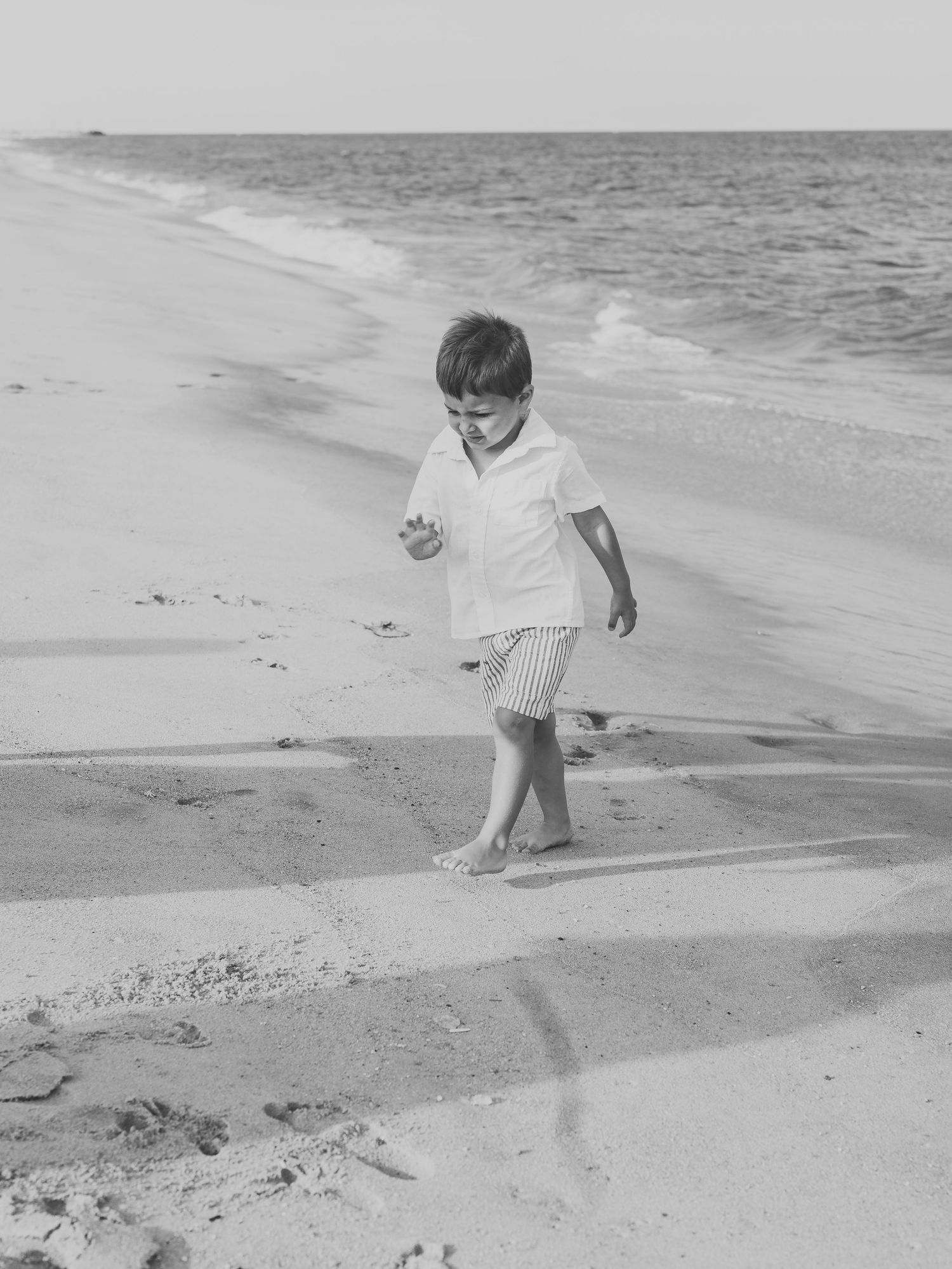 Four year old boy runs from the ocean waves in a black and white photo.
