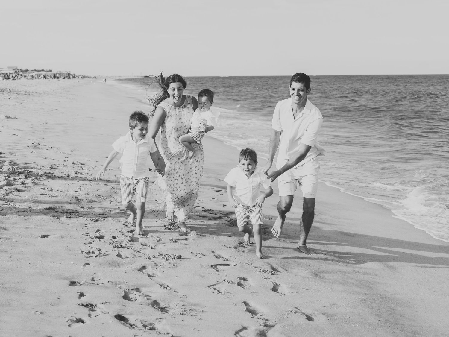 Black and white image of Parents holding their young children on the beach in Point Pleasant during golden hour.