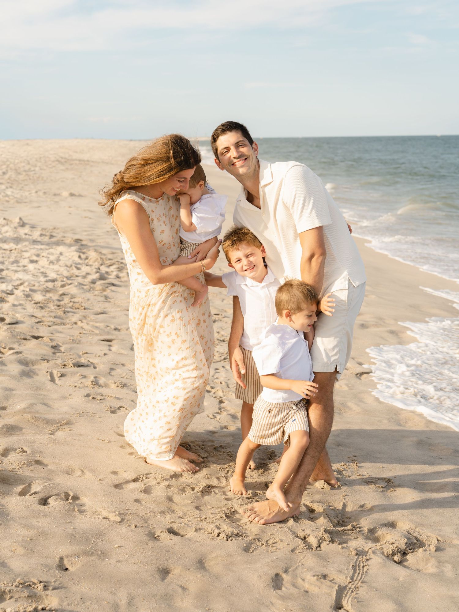 Family of five with all sons snuggle together laughing on the bay head beach.