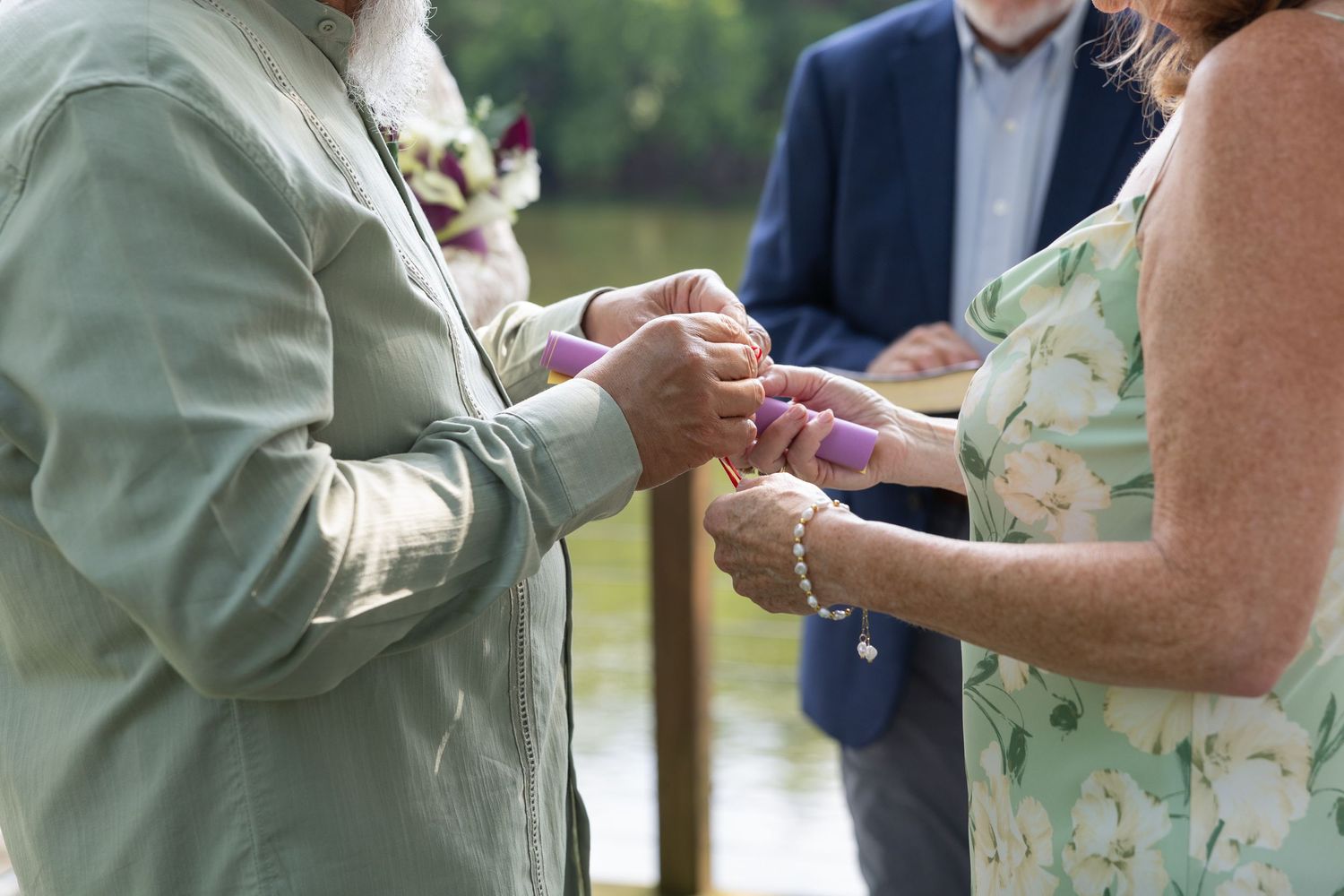 Couple exchanging rings during an outdoor wedding ceremony with guests in the background.