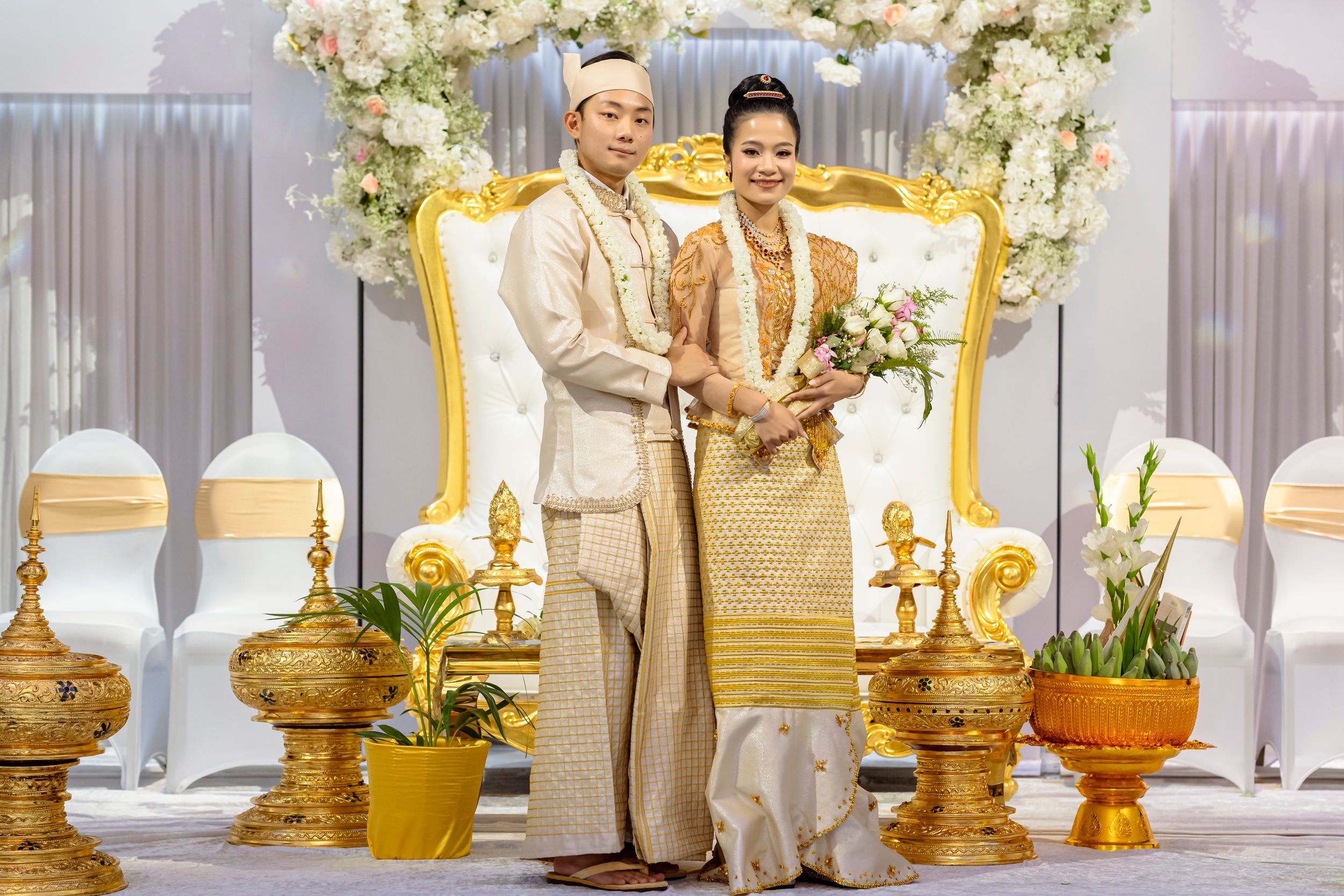 Traditional Cambodian wedding ceremony with couple in gold attire praying at ornate altar with golden decorations.